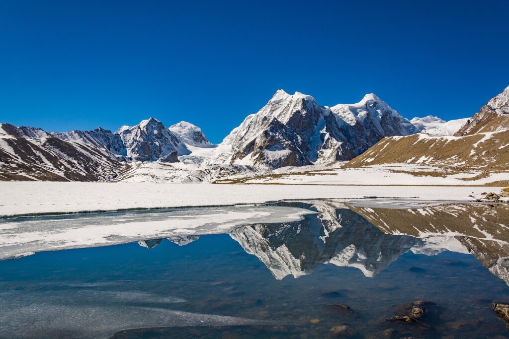 Gurudongmar Lake, one of the most breathtaking Places to Visit in Sikkim, featuring crystal-clear turquoise waters surrounded by snow-capped Himalayan mountains under a bright blue sky.